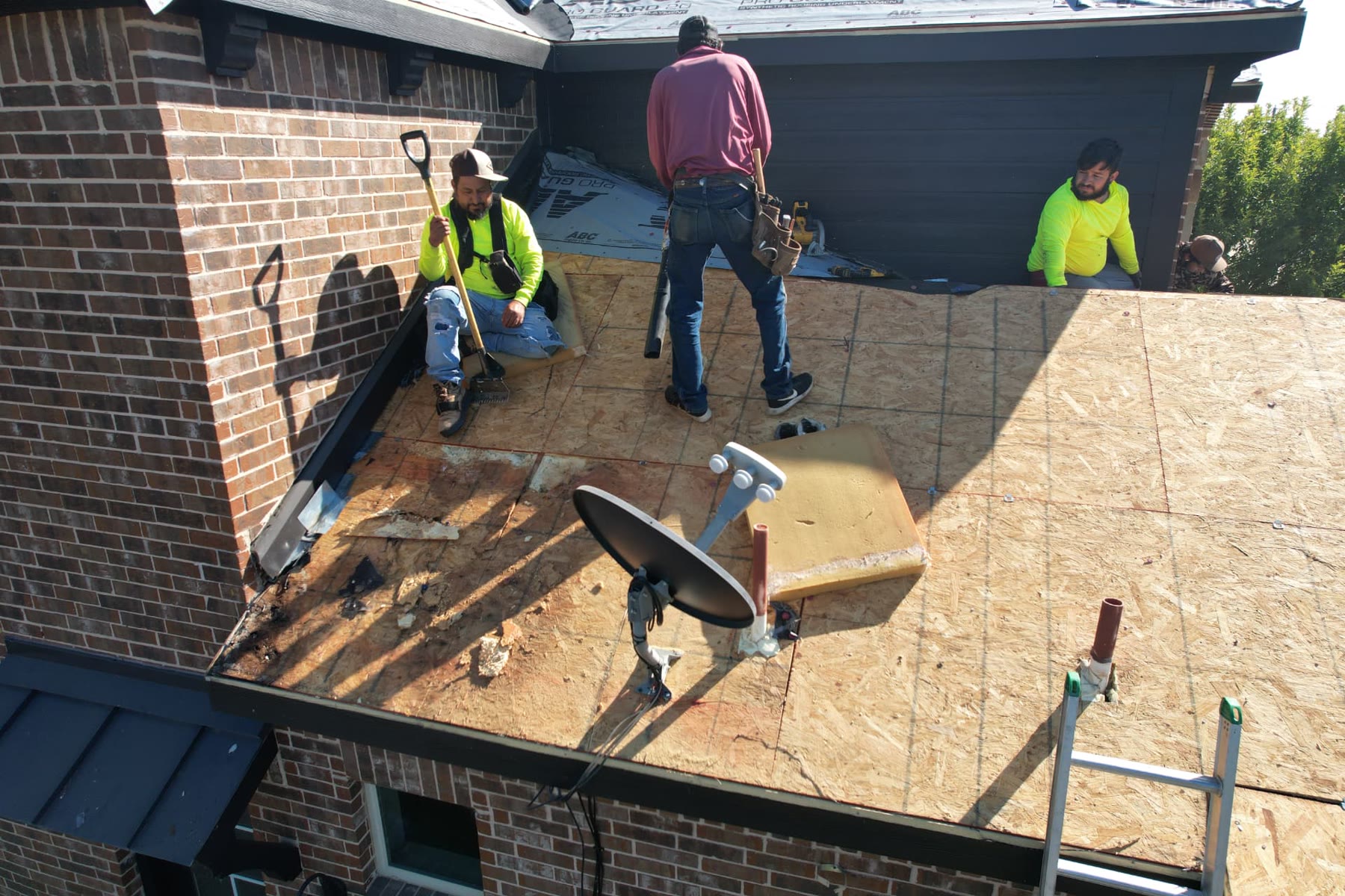 Roofing crew tearing off old shingles down to the decking on a black-sided DFW home