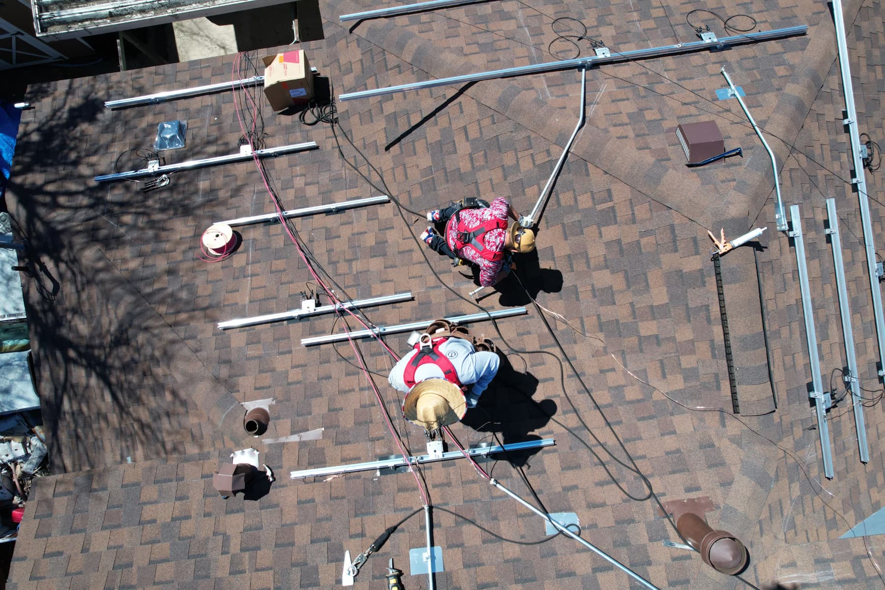 Aerial photo of two roofers working across brown architectural shingles with mounting rails staged on the roof