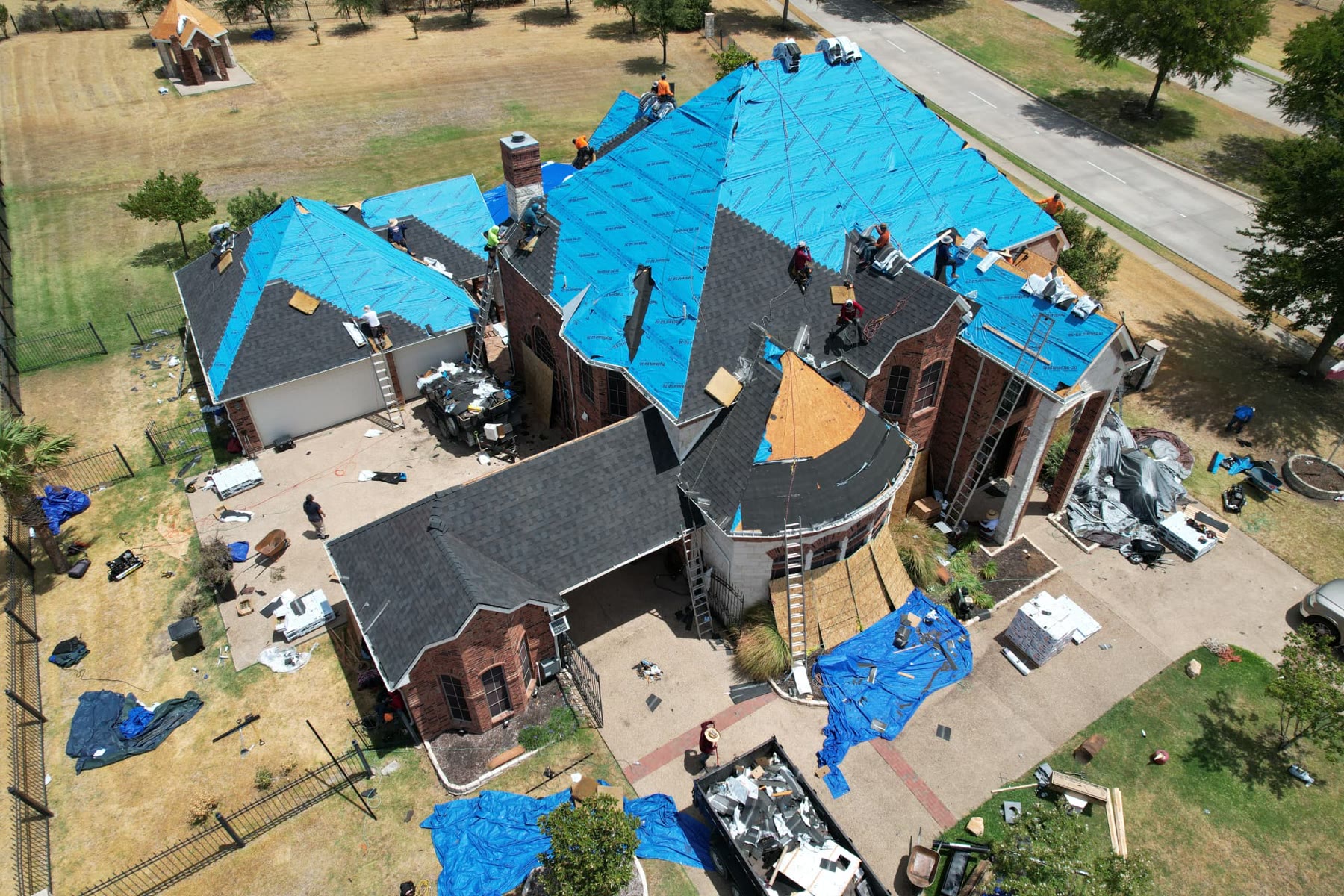 Aerial view of a large DFW home mid roof replacement with blue synthetic underlayment and the Max Exteriors crew working
