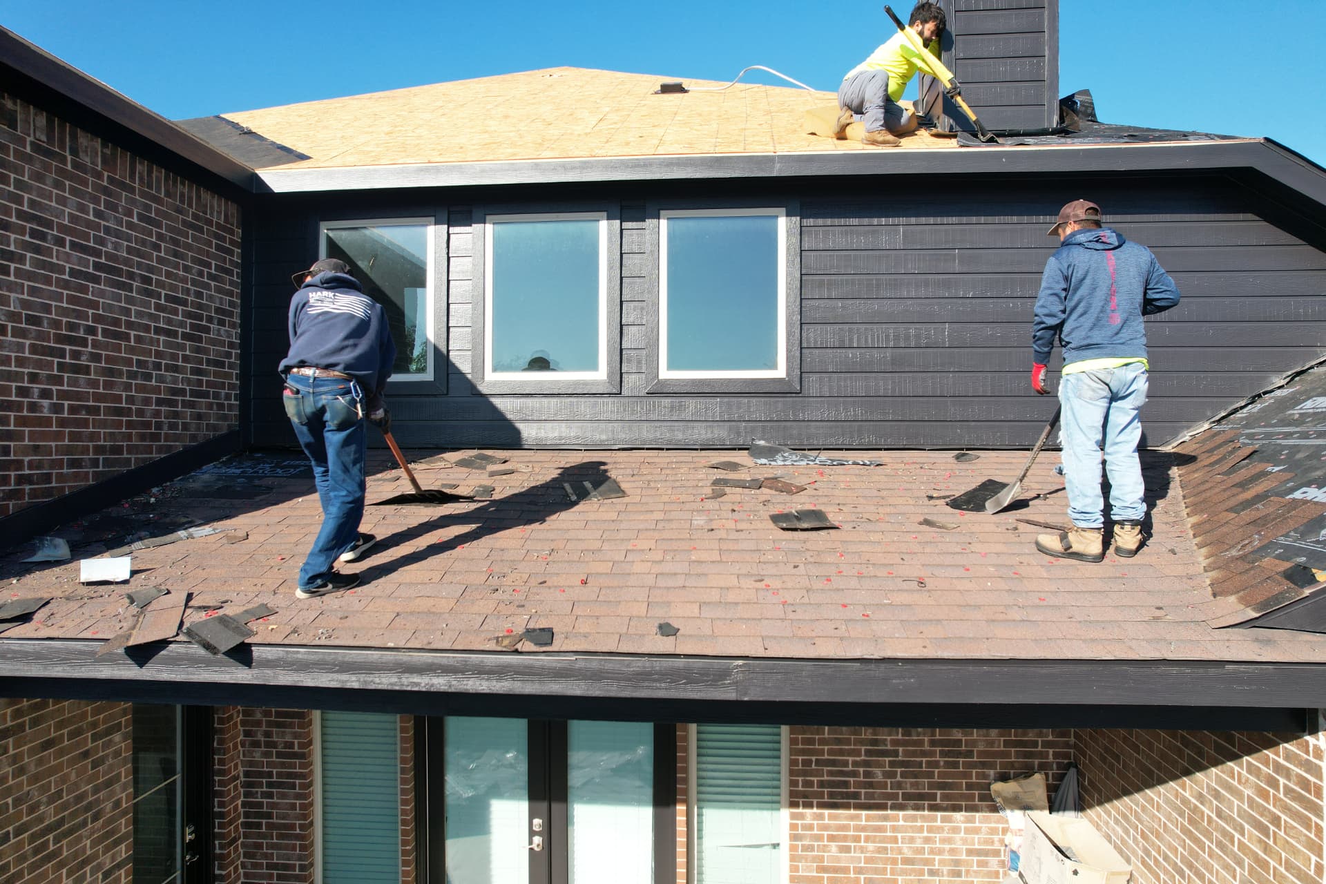 Three-person crew shoveling old shingles off a residential roof down to fresh decking